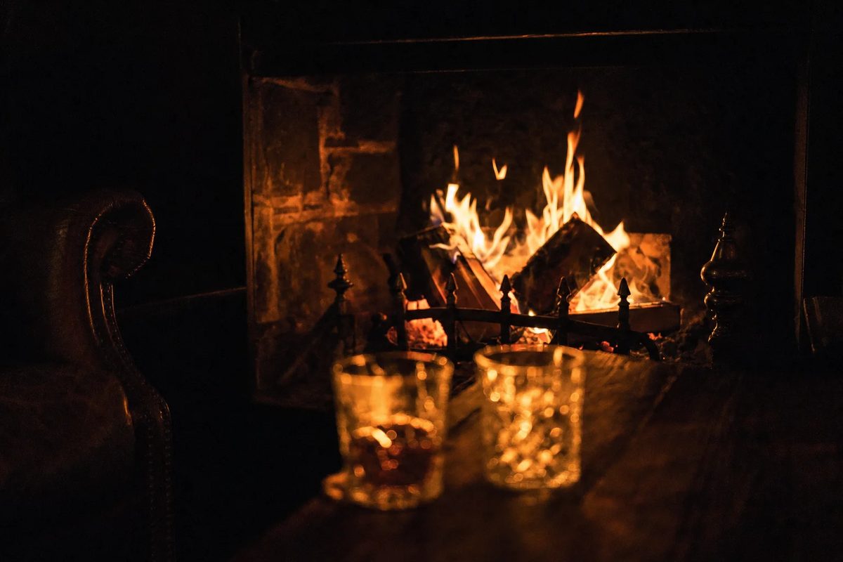 A log fire burning in a brick hearth, two cut-glass tumblers on the table in front of it.